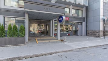 Ingresso moderno di un hotel con insegna blu che indica il servizio alberghiero, il numero 1214 e un idrante visibile sul marciapiede.