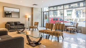 Un moderno vestíbulo de hotel con una mesa de centro de vidrio, sillones a rayas, un sofá y un espejo grande.