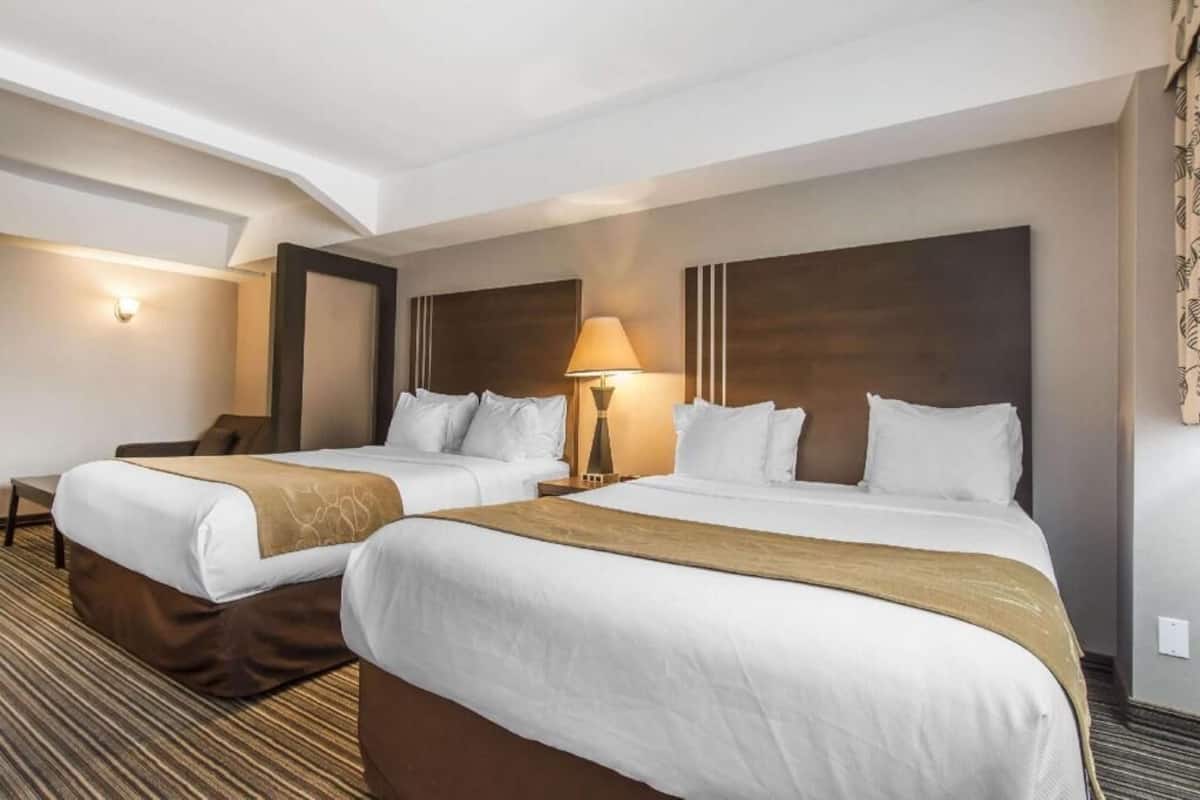 Habitación de hotel con dos camas, un escritorio, una silla, una lámpara y una luz en la pared.