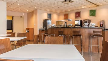 Un comedor moderno con una barra central, mesas blancas y sillas de madera.