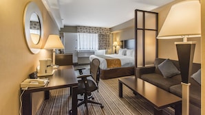 Habitación de hotel con cama, escritorio, silla, sofá, lámpara, espejo y ventana con cortinas.