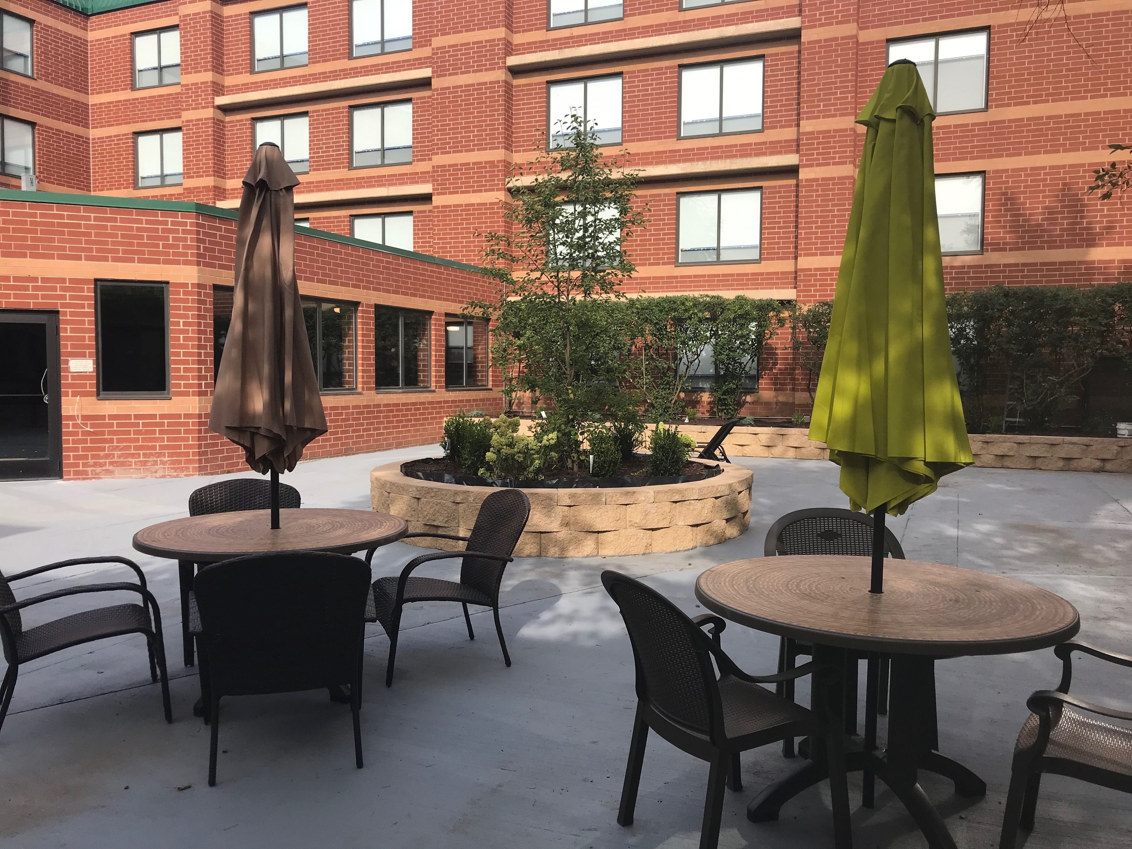 An outdoor patio with round tables and chairs, surrounded by a brick building with multiple windows.
