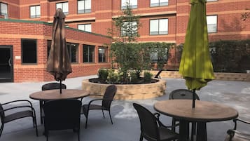 An outdoor patio with round tables and chairs, surrounded by a brick building with multiple windows.