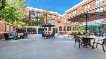A courtyard with outdoor seating, including tables and chairs, and umbrellas providing shade.