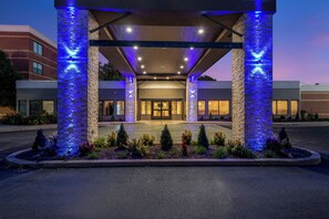 A hotel entrance with a covered walkway, stone pillars, and a landscaped area with plants.