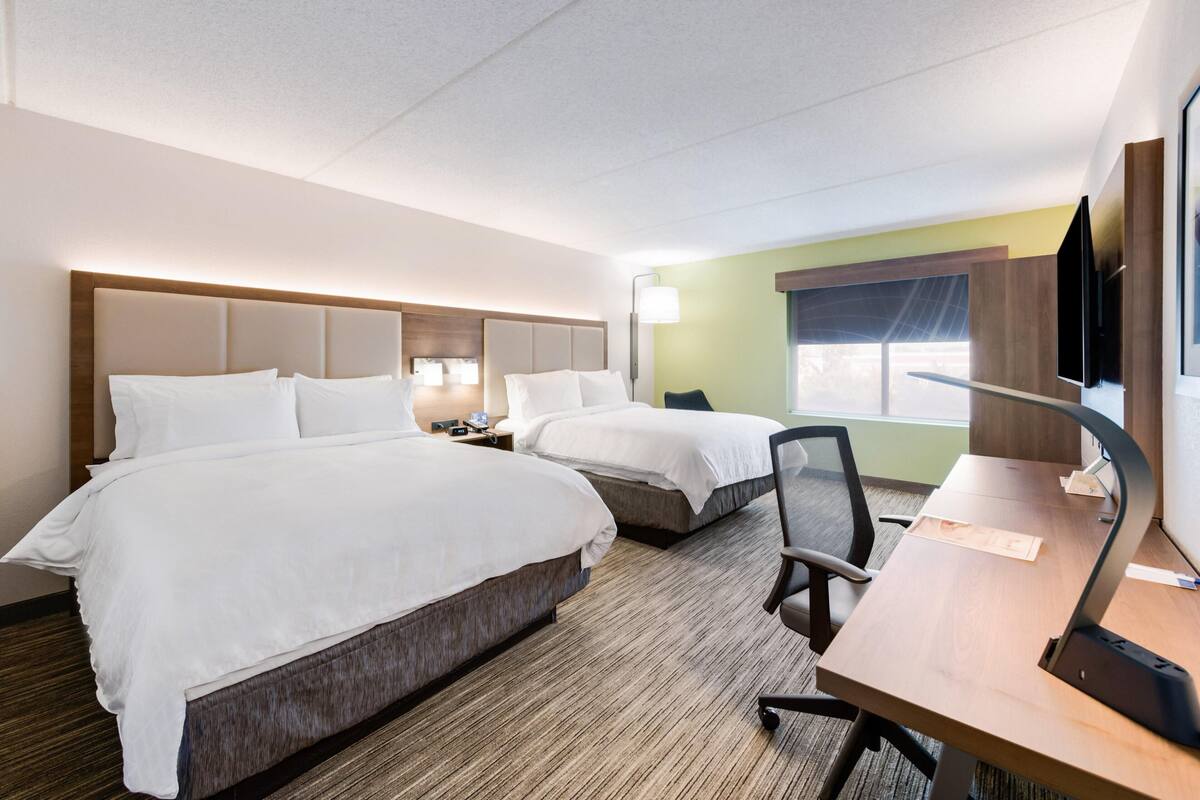 A hotel room with two beds, a desk, a chair, and a TV.