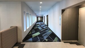 A long, narrow hotel corridor with patterned carpet, light wooden flooring, and a series of doors on one side. - Holiday Inn Express Naperville by IHG (Naperville)