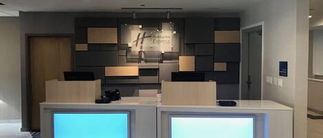 Un mostrador de recepción de hotel con diseño moderno, con dos mostradores iluminados y un letrero en la pared que dice "Holiday Inn Express".