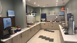 A modern kitchen area with a fruit dispenser, a bakery section, and a counter with various kitchen utensils. - Holiday Inn Express Naperville by IHG (Naperville)