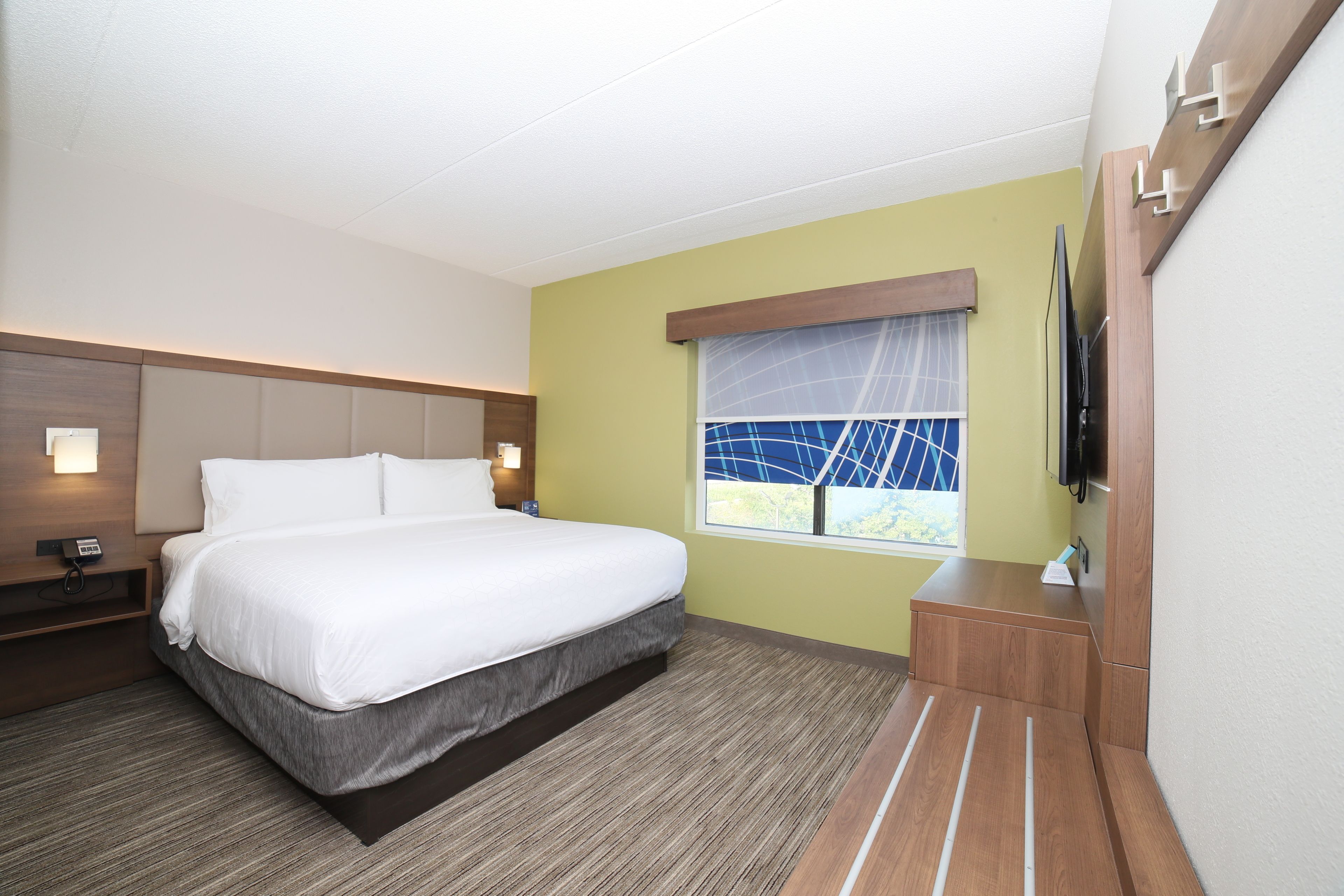 A hotel room with a large bed, a bedside table, a TV, and a window with a view.