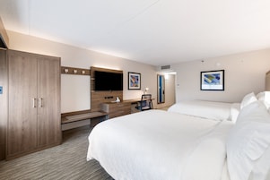 A hotel room with a large bed, a desk with a chair, a wardrobe, and two framed pictures on the wall.