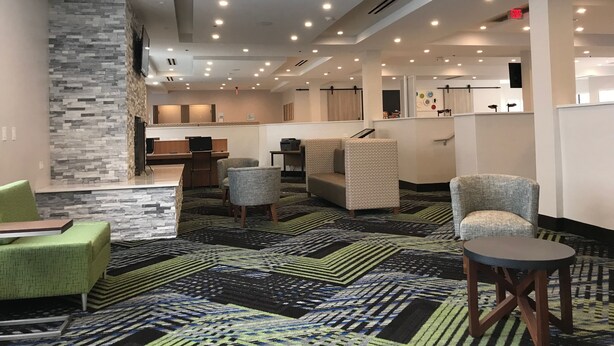 A hotel lobby with a modern design, featuring a stone accent wall, multiple seating areas, and a patterned carpet. - Holiday Inn Express Naperville by IHG (Naperville)
