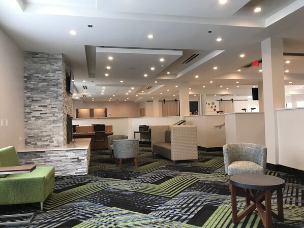 A hotel lobby with a modern design, featuring a stone accent wall, multiple seating areas, and a patterned carpet. - Holiday Inn Express Naperville by IHG (Naperville)