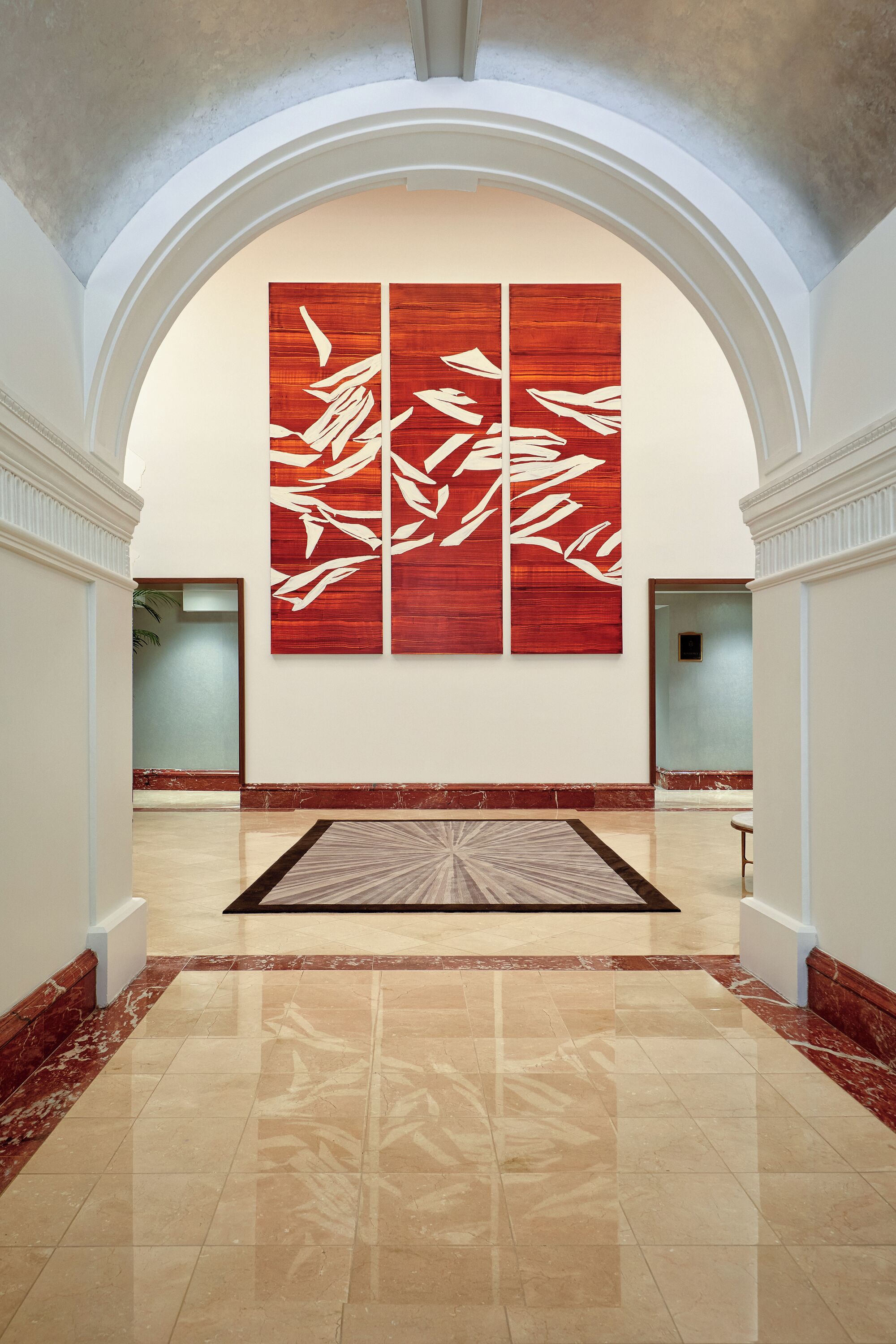 Un hall d’entrée spacieux, agrémenté d’un grand tableau abstrait rouge, de sols en marbre poli et d’un plafond en arc de style classique.