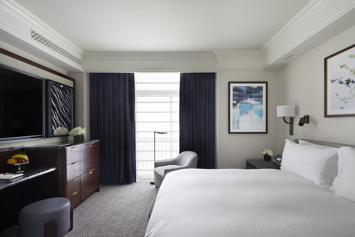 A hotel room with a large bed, a desk with a TV, a chair, and a painting on the wall.