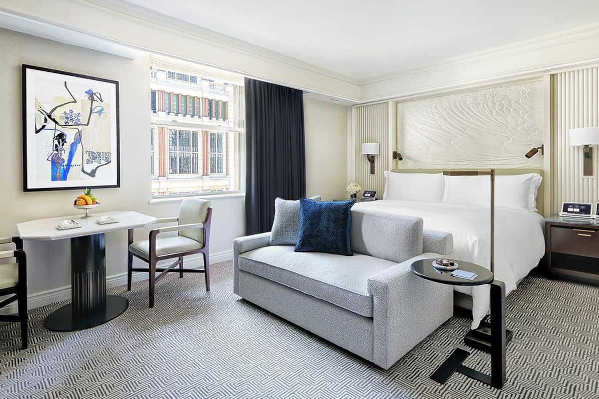 A hotel room with a bed, a sofa, a desk, and a window with curtains.