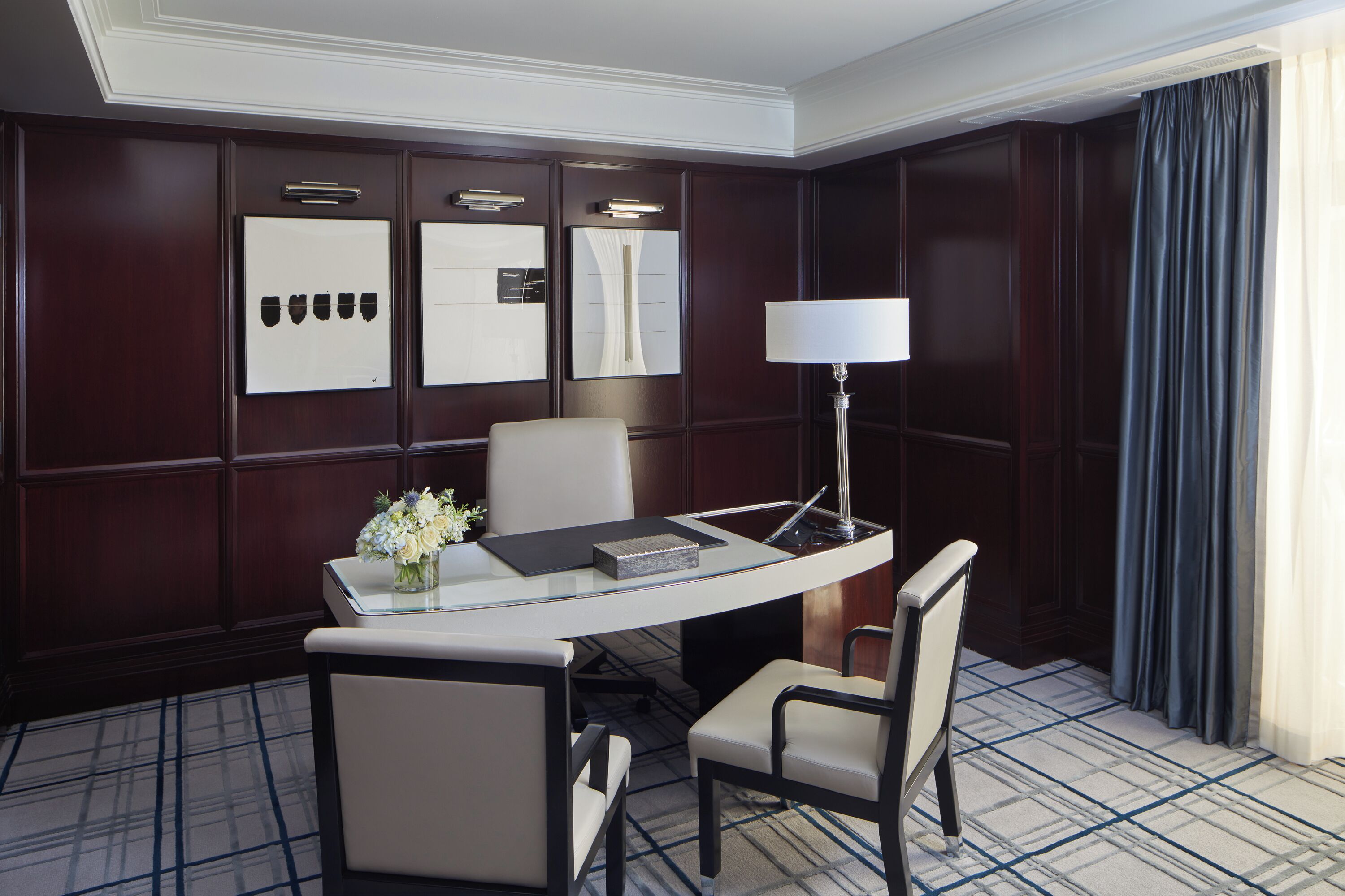 A hotel room with a large desk, two chairs, a lamp, and a mirror.