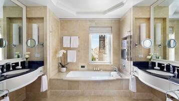 A luxurious bathroom with two sinks, a large bathtub, and a window with a city view.