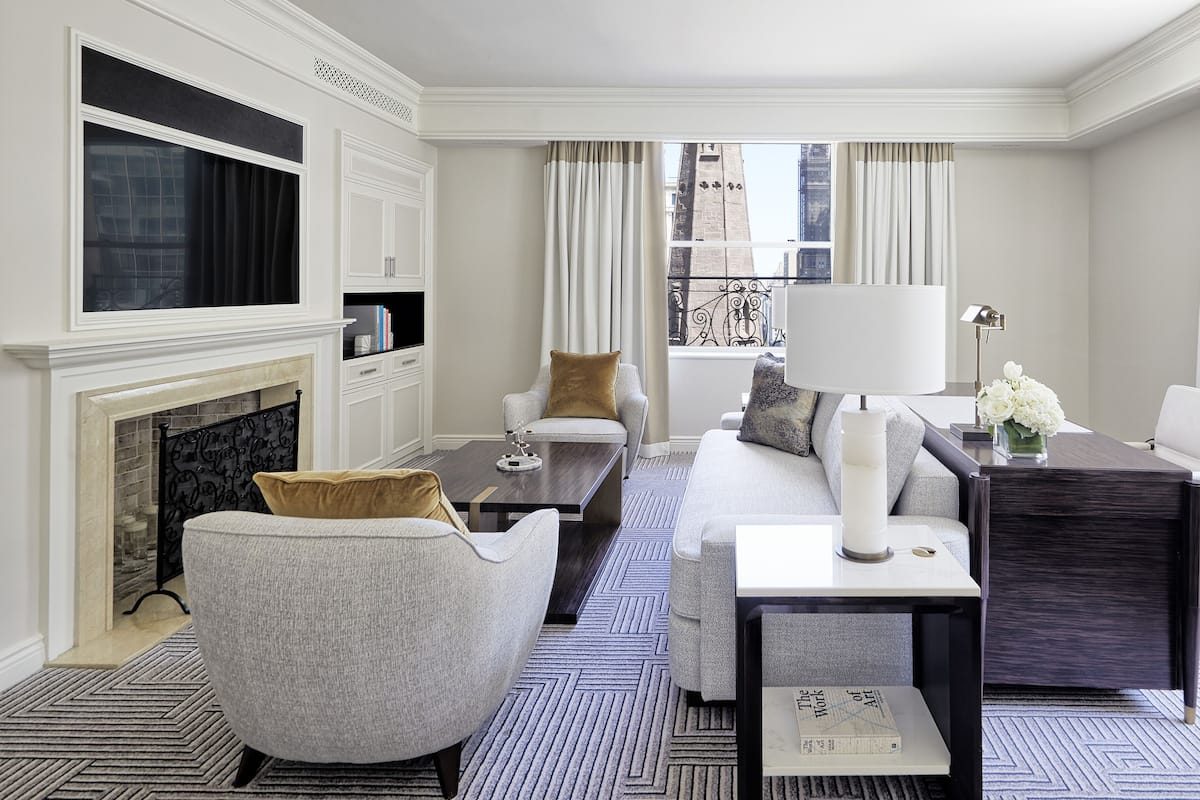 A modern living room with a fireplace, a sofa, a coffee table, and a side table with a lamp and flowers.