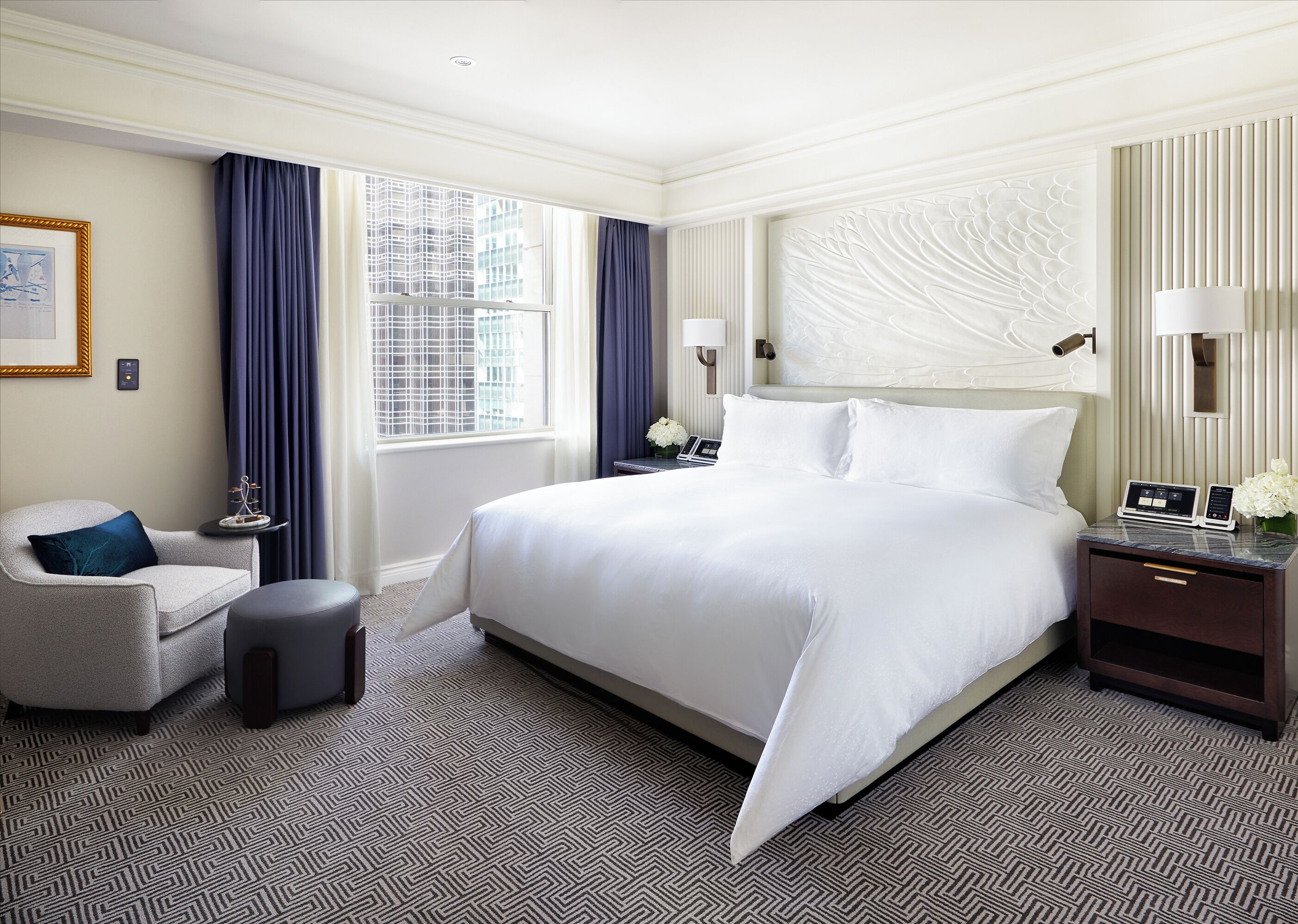 Ein Hotelzimmer mit einem großen Bett, einem Sessel, einem Nachttisch und einem Fenster mit Vorhängen.
