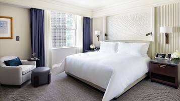 Ein Hotelzimmer mit einem großen Bett, einem Sessel, einem Nachttisch und einem Fenster mit Vorhängen.
