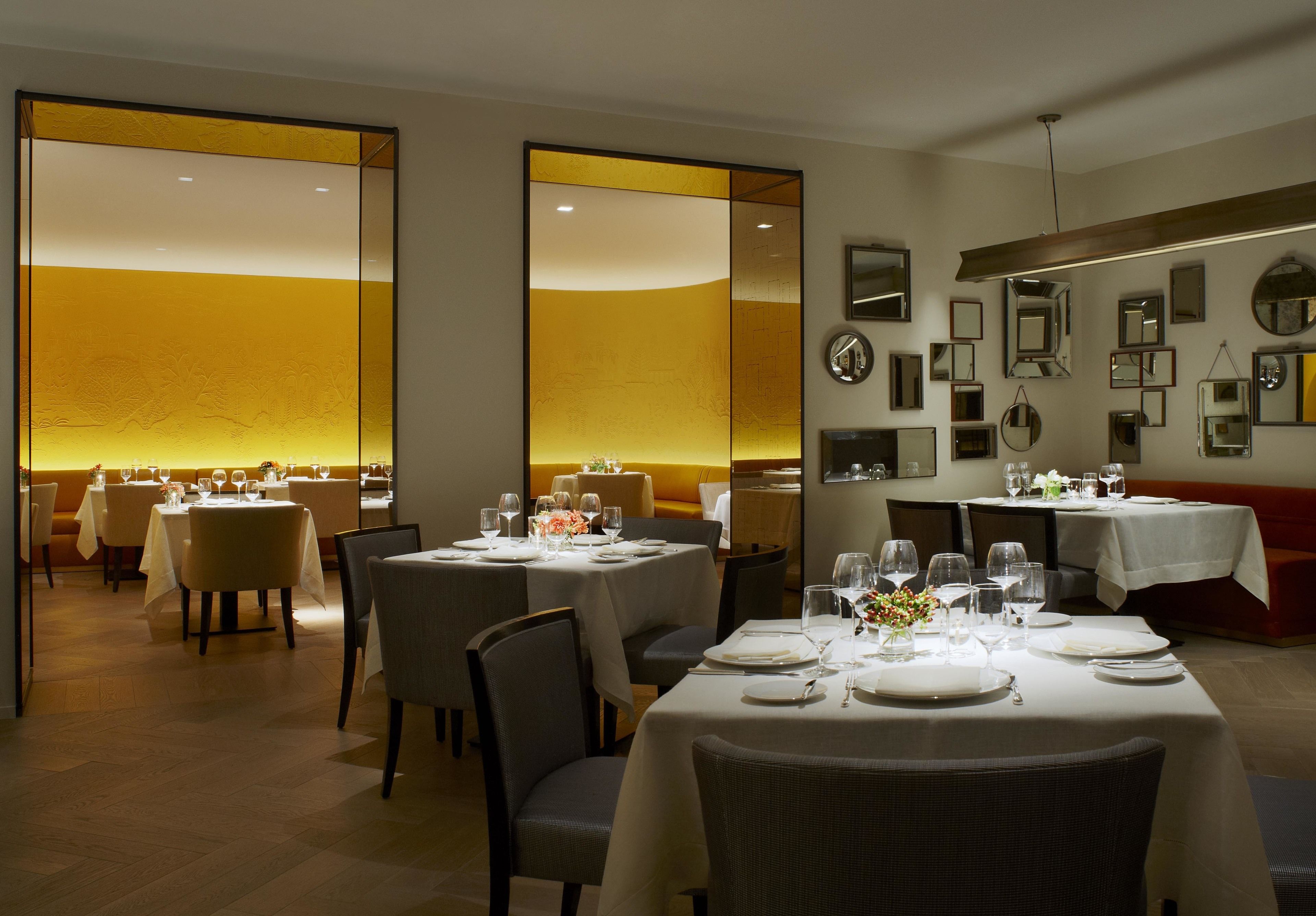 A restaurant with tables set for dining, a mirror wall, and a warm ambient light.