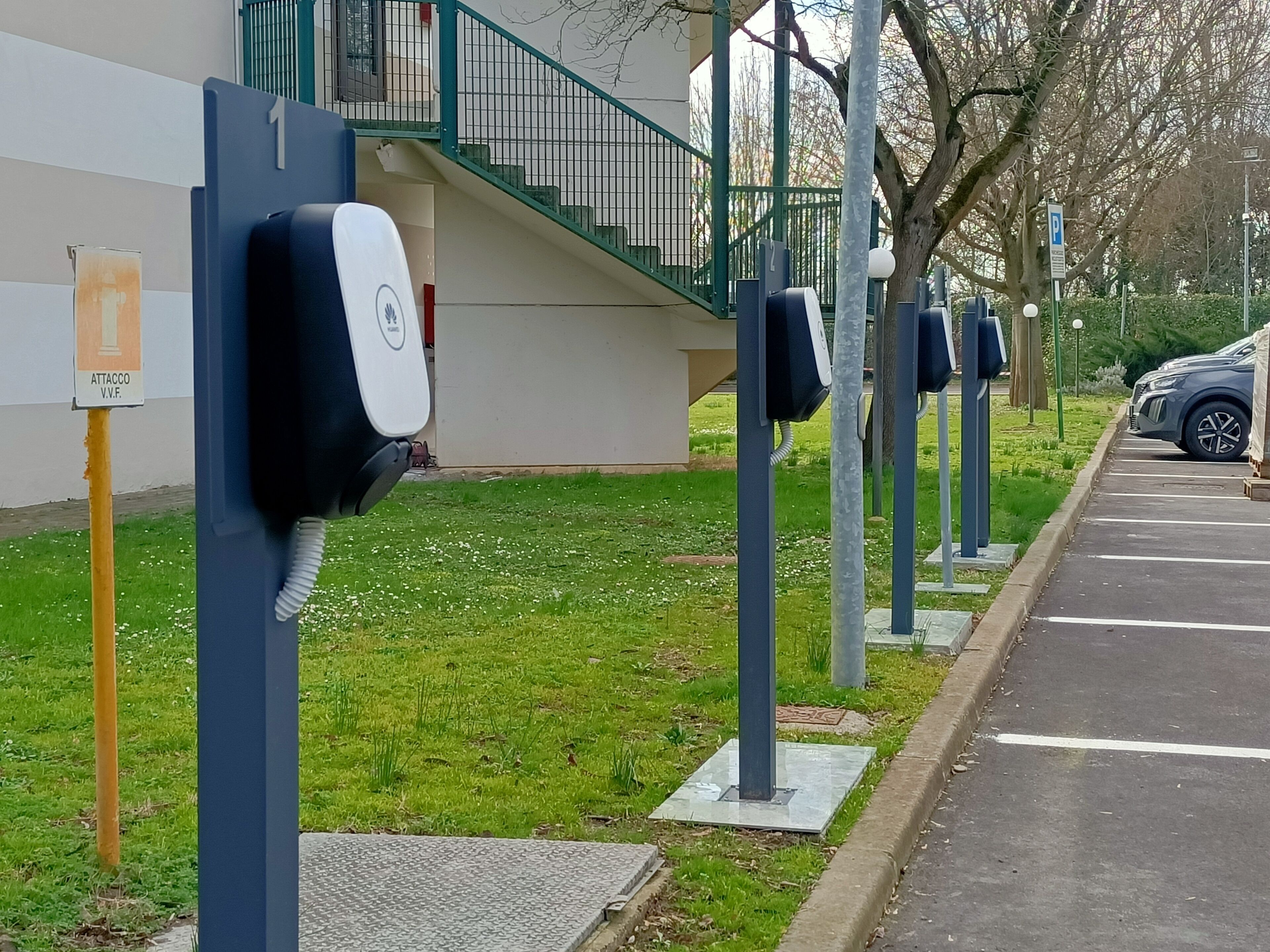 A row of electric vehicle charging stations along a sidewalk next to a building with a staircase.