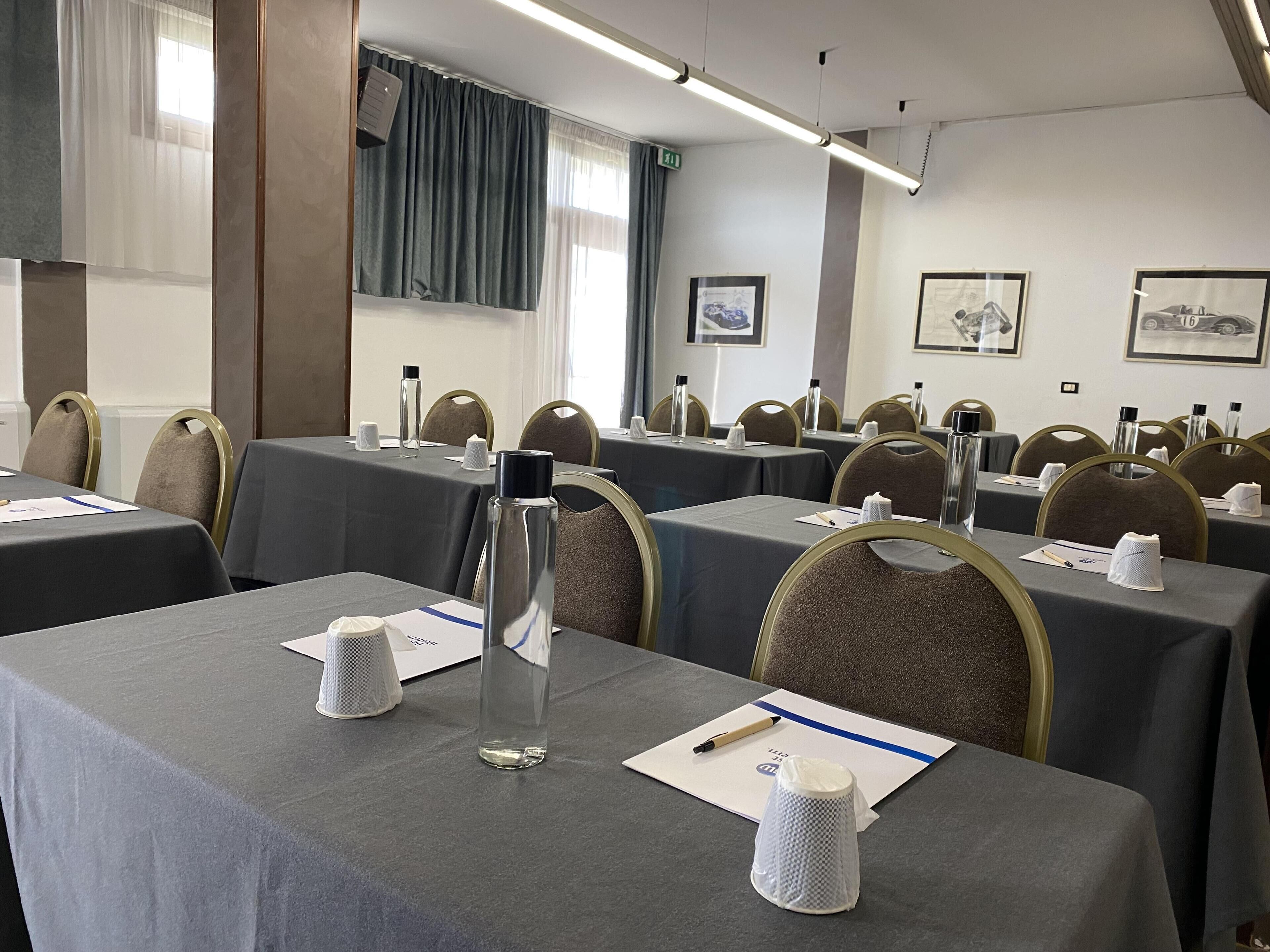 Ett konferensrum med bord uppställda för möten, utrustat med vattenflaskor, anteckningsblock och pennor.