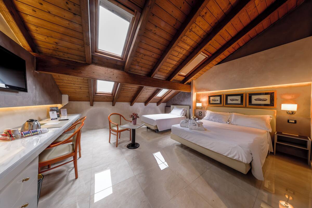Ein Hotelzimmer mit Holzboden, einem Bett, einem Schreibtisch mit Stuhl, einem kleinen Tisch mit Pflanze und einem Fernseher.