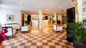 A hotel lobby with a checkered floor, reception desk, seating area, and decorative plants.