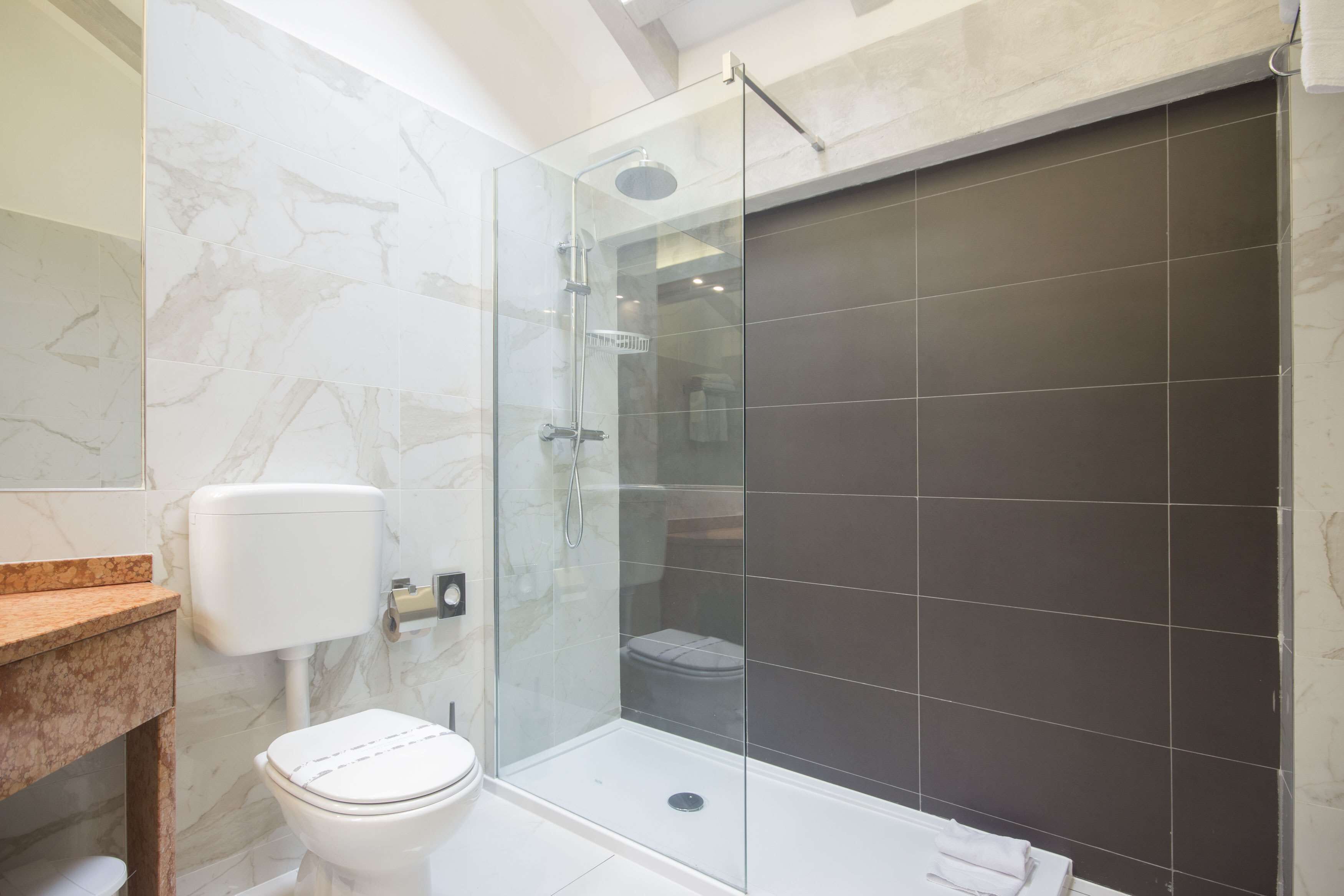 A modern bathroom with a glass-enclosed shower, a toilet, and a marble-tiled wall.