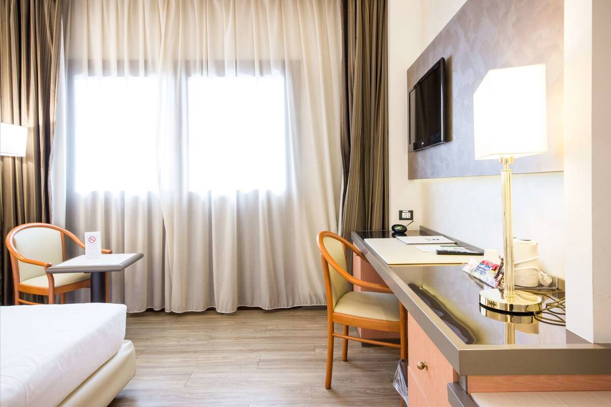 Ein Hotelzimmer mit einem Bett, einem Schreibtisch, einem Sessel, einem Fernseher und einer Lampe.