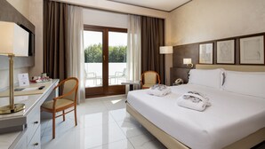 A hotel room with a bed, desk, chairs, and a view through the glass door.
