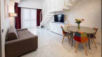 Ein modernes Wohnzimmer mit einer Couch, einem Esstisch mit bunten Stühlen, einem Flachbildfernseher und einer Treppe.