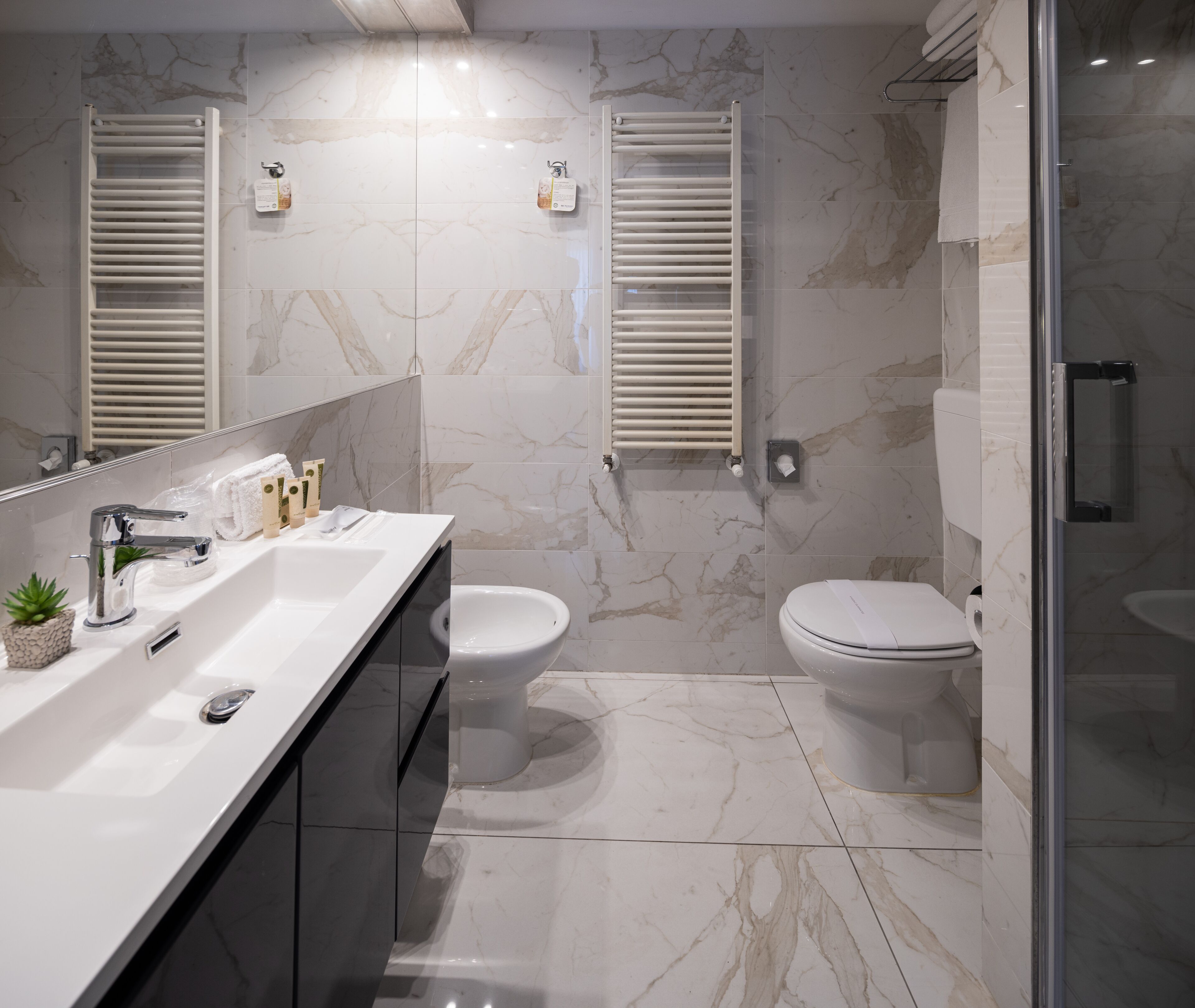 A modern bathroom with a marble floor, two toilets, a sink with a mirror, and a shower area.