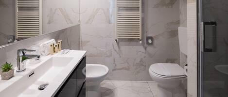 A modern bathroom with a marble floor, two toilets, a sink with a mirror, and a shower area.