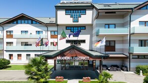 A hotel with a central entrance, multiple flags, and a sign reading "MODENA DISTRICT".