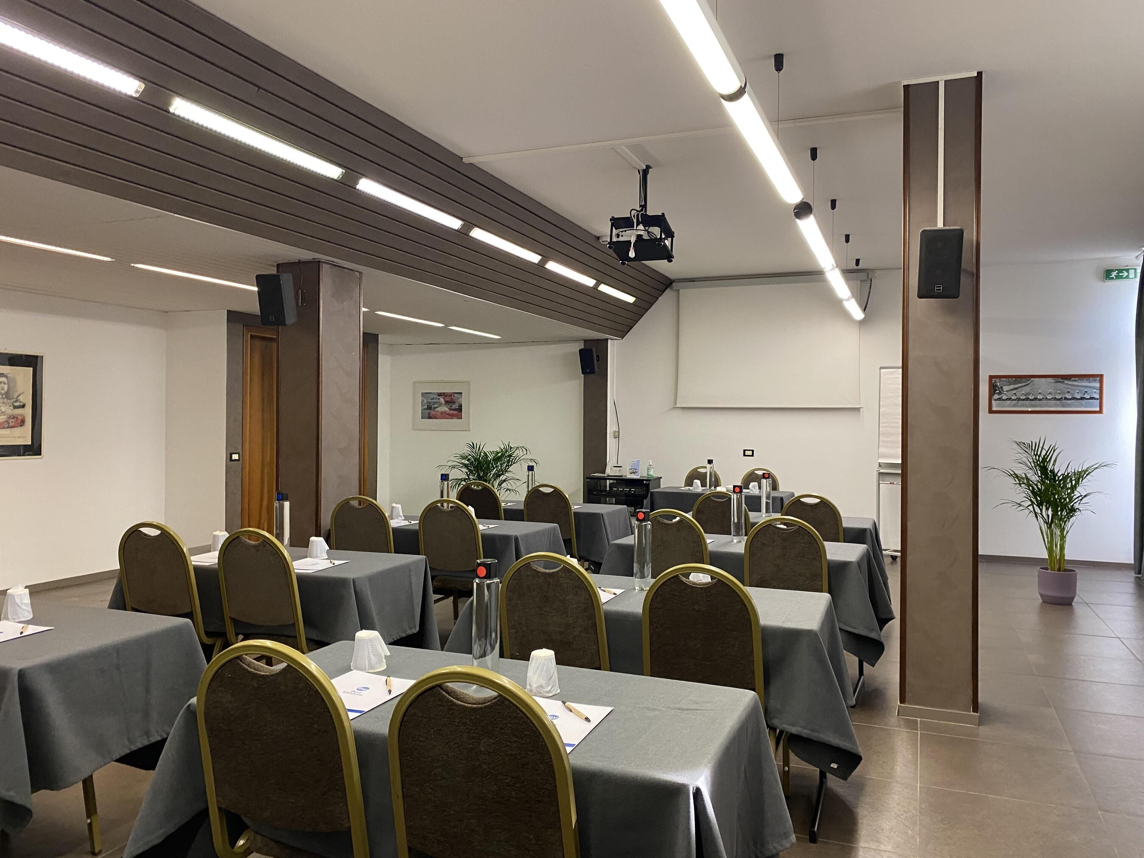 A conference room with tables and chairs, a projector, and a screen.