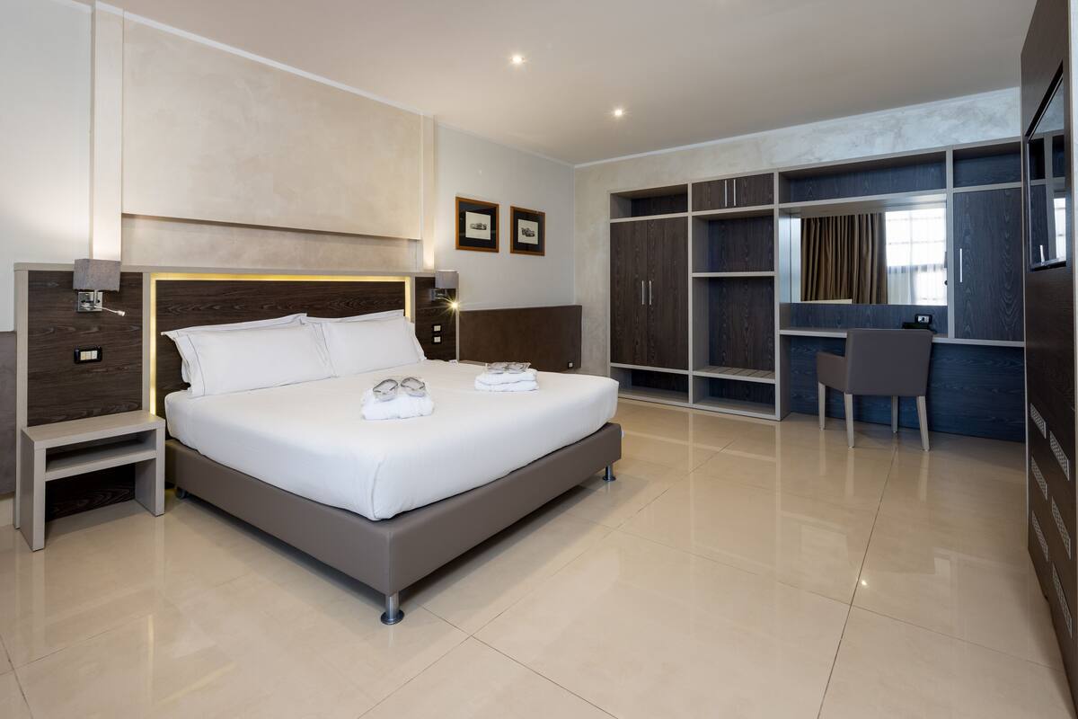 Ein modernes Hotelzimmer mit einem großen Bett, Nachttischen, einem Schreibtisch und einem begehbaren Kleiderschrank.