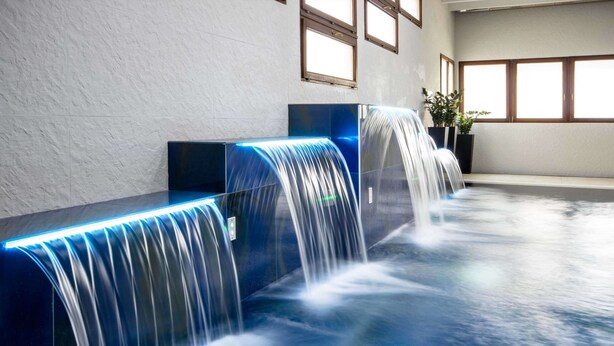 A modern indoor pool area with multiple water features and seating areas.