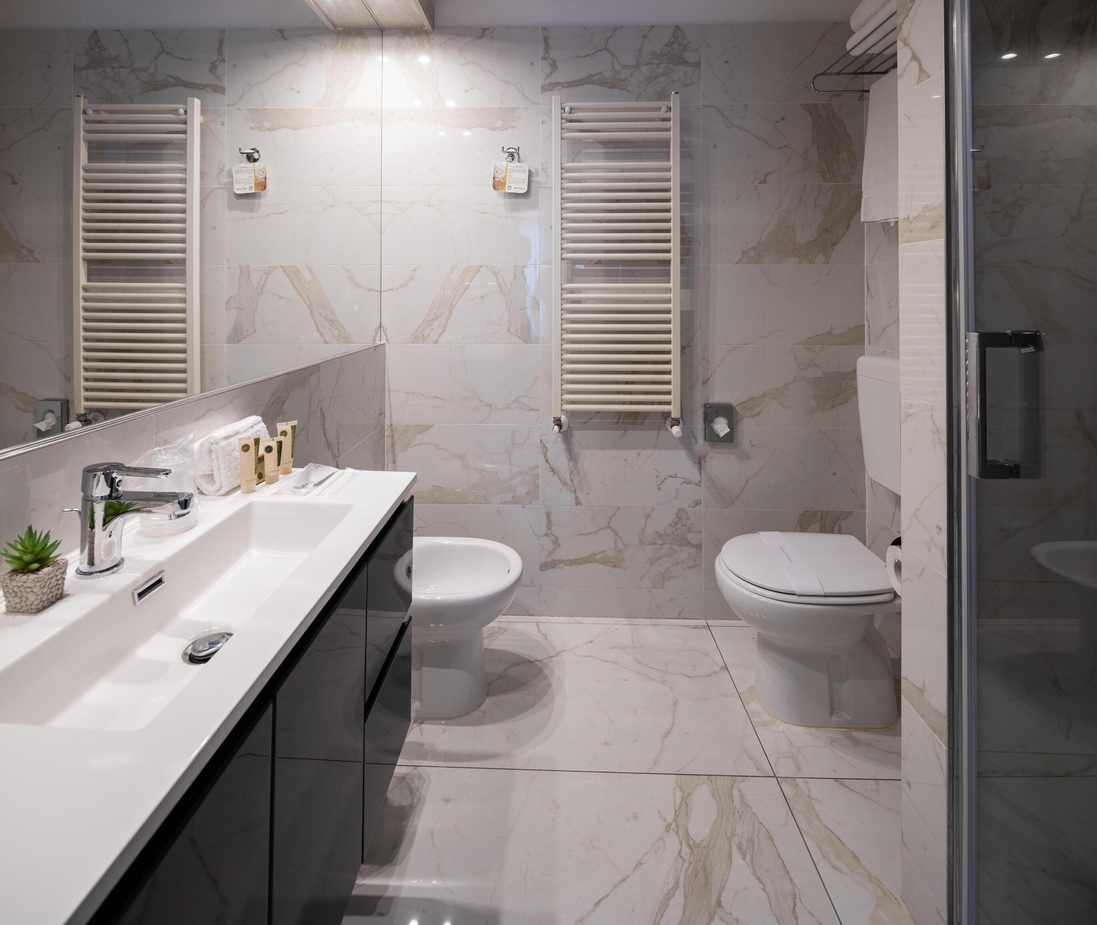 A modern bathroom with a white sink, two toilets, a shower area, and marble flooring.