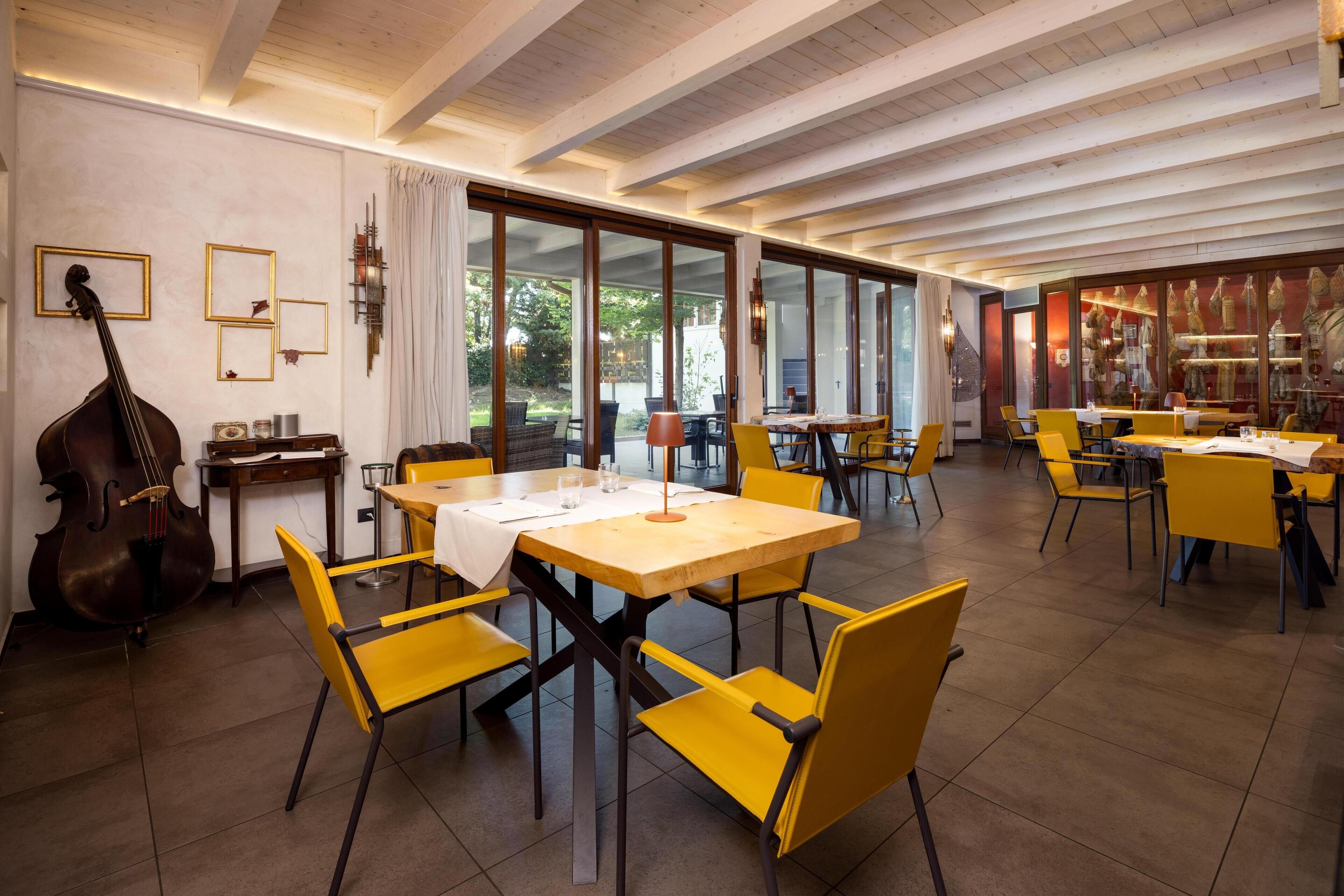 A spacious dining area with yellow chairs and tables, large windows, and a wooden ceiling.