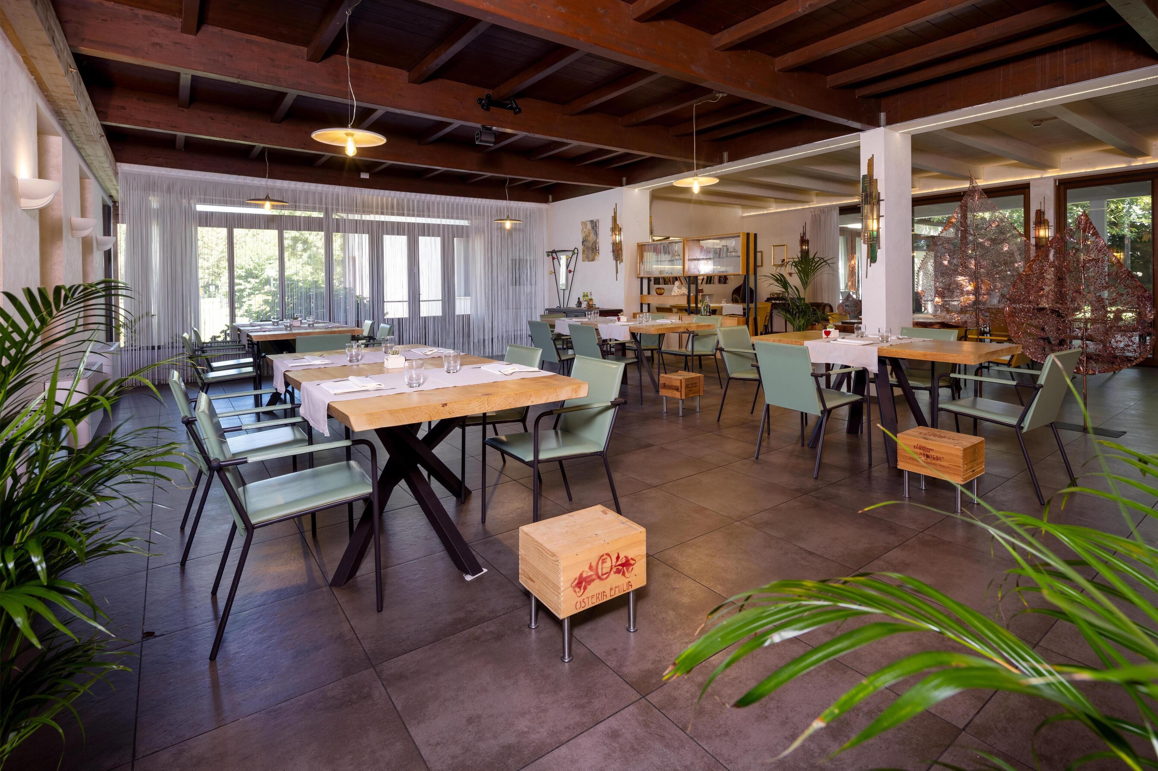 A spacious dining area with multiple tables and chairs, large windows, and a high ceiling with exposed beams.