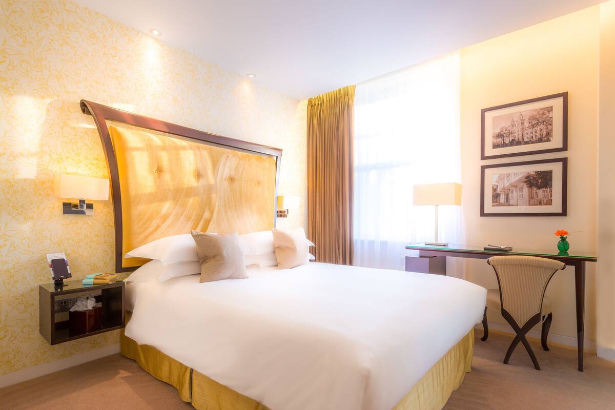 A hotel room with a large bed, a desk, a chair, and two framed pictures on the wall.