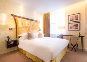 A hotel room with a large bed, a desk, a chair, and two framed pictures on the wall.
