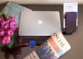 A laptop, a smartphone, a watch, a magazine, and a bouquet of pink roses on a table.