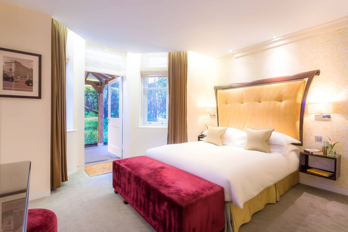 A spacious bedroom with a large bed, a red bench, a nightstand with a lamp, and a framed picture on the wall.