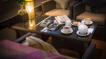 A cozy seating area with wicker furniture, a table with a newspaper, a teapot, cups, and a plant.
