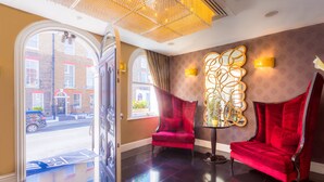 A lobby with a red velvet chair, a decorative wall piece, and a view of the street outside.