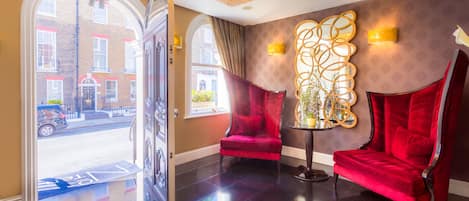 A lobby with a red velvet chair, a decorative wall piece, and a view of the street outside.